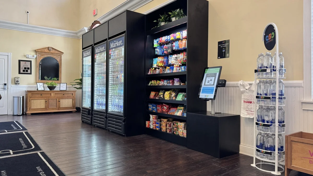 Lobby market with refrigerated drinks, snack shelves and a self-checkout terminal.